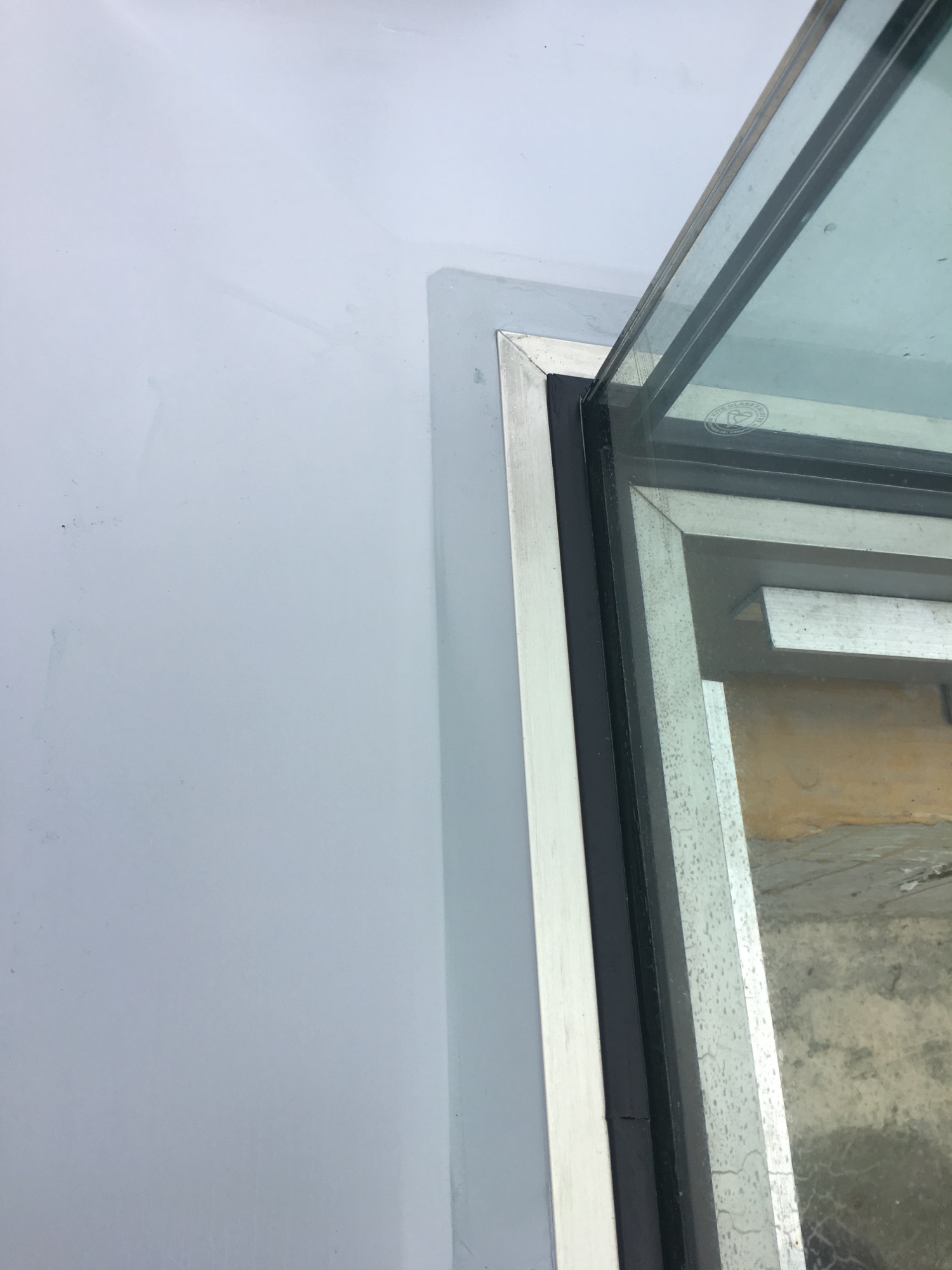 Close-up of a glass window corner with a metal frame against a wall.
